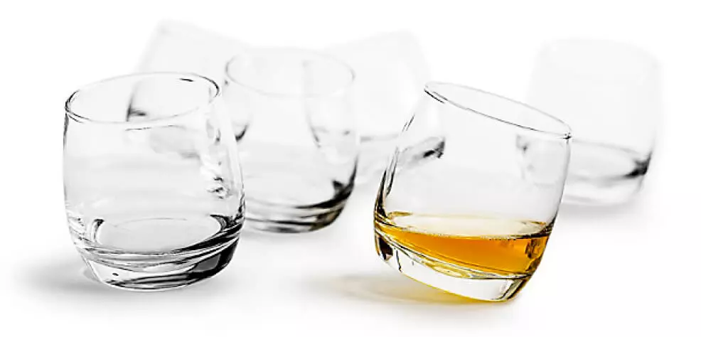 Six whisky glasses on a white background, one of them with whisky in and slightly tilted