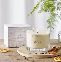 A large White Company Candle lit and resting on a wooden table
