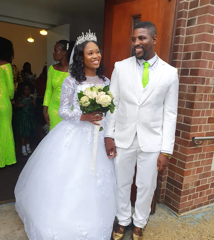 A woman wearing a beautiful white wedding dress holding flowers and a man in a white suit with a bright green tie.